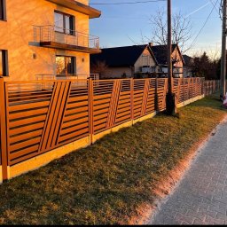 FusionWW - Nowoczesne ogrodzenie poziome z elementami ukośnymi, wykonane z brązowych desek na betonowej podmurówce, w tle dom jednorodzinny.