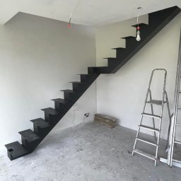 FusionWW - Nowoczesne, czarne schody metalowe wspornikowe w surowym wnętrzu, z widoczną drabiną i przewodami elektrycznymi zwisającymi z sufitu. Minimalistyczny design.