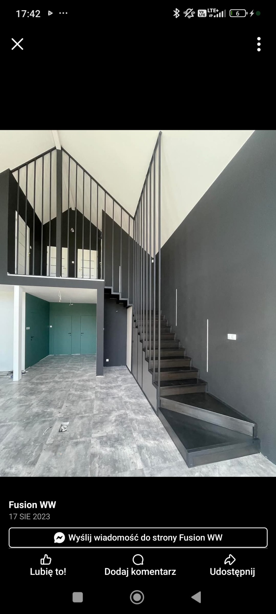 Nowoczesne, czarne schody metalowe z ażurową balustradą w loftowym wnętrzu. Minimalistyczny design, szara podłoga, zielone drzwi w tle.