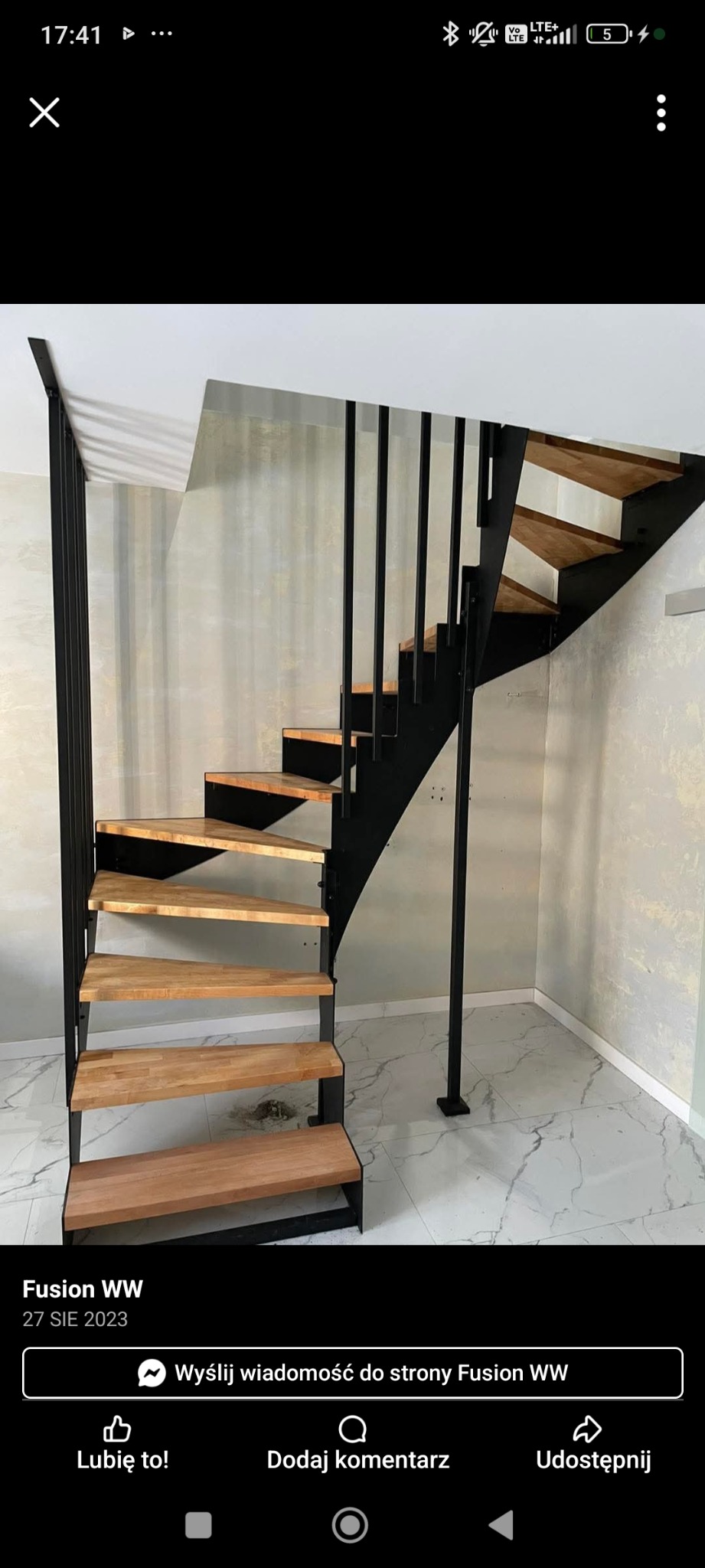 Nowoczesne schody metalowe z drewnianymi stopniami, czarna konstrukcja, jasne tło. Widok z dołu ukazuje solidne wykonanie i minimalistyczny design.