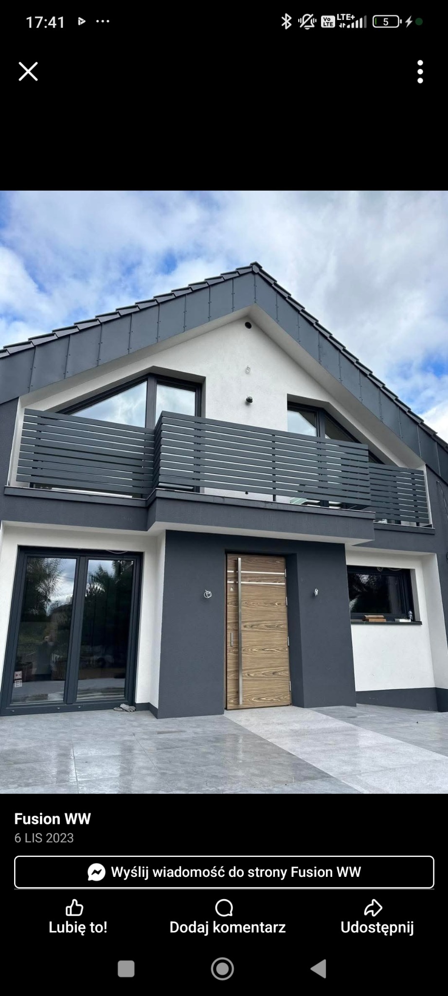 Nowoczesny dom z szarą, horyzontalną balustradą balkonową i drewnianymi drzwiami wejściowymi. Elewacja w odcieniach szarości i bieli. Minimalistyczny design.