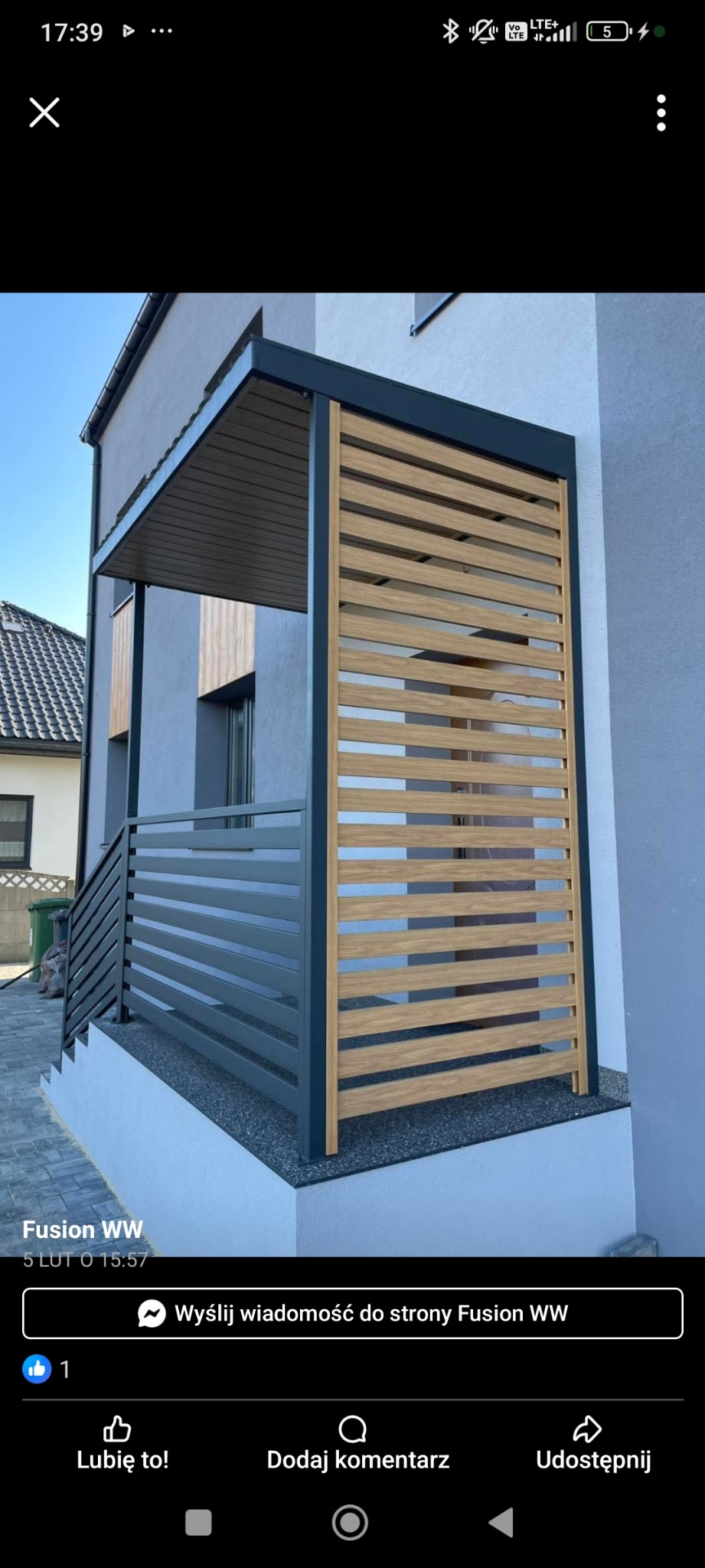 Nowoczesna zabudowa balkonu z drewnianymi lamelami i szarą metalową konstrukcją, widoczna z zewnątrz budynku. Minimalistyczny design i stonowana kolorystyka.