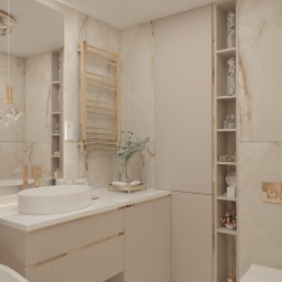 Design by Blonde Agnieszka Buszman - Elegancka łazienka w beżach: marmurowe ściany, owalna umywalka na szafce z frezowanymi frontami, złote akcenty, dekoracyjne półki z bibelotami i kwiatami.