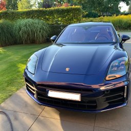 PureSteam Radosław Lange - Błyszczący, granatowy samochód osobowy marki Porsche zaparkowany na kostce brukowej, z widocznym wężem i zielenią w tle.