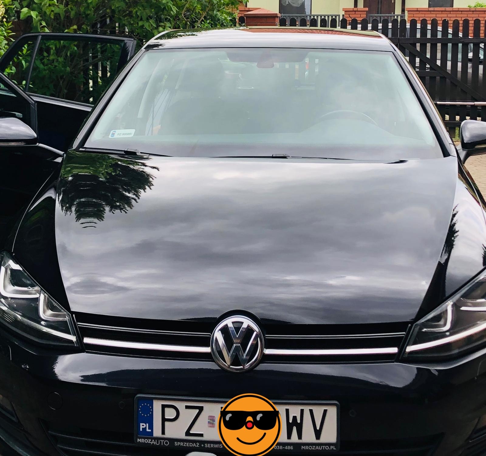 Błyszczący, czarny Volkswagen Golf z otwartymi drzwiami kierowcy, zaparkowany na zewnątrz. Widoczne odbicia w karoserii i tablica rejestracyjna z przodu.