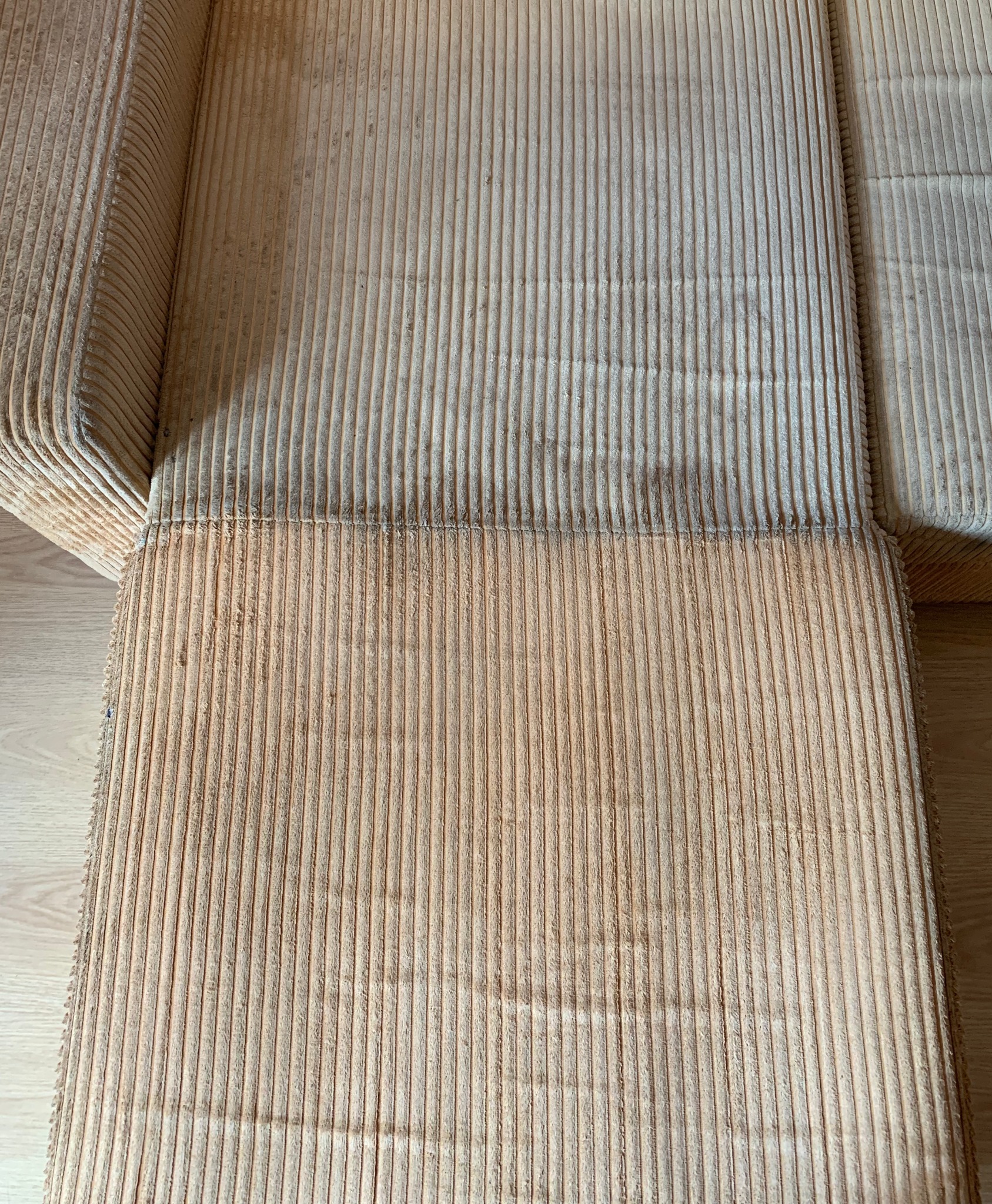 Częściowo wyczyszczona, beżowa kanapa z tkaniny prążkowanej w Poznaniu. Widoczna różnica w kolorze między czystą a brudną częścią tapicerki.