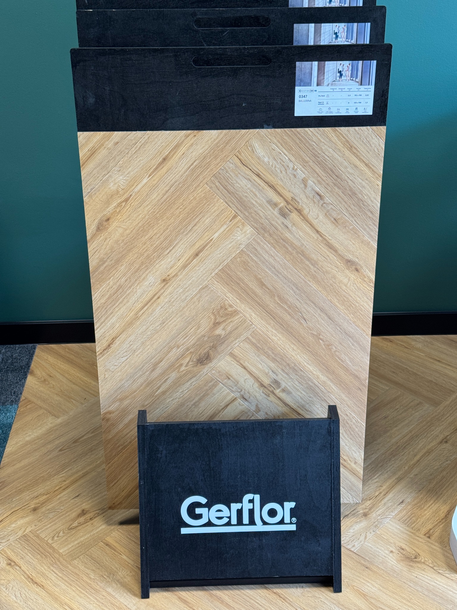 Prezentacja próbki paneli Gerflor ułożonych we wzór jodełki, z widoczną specyfikacją techniczną i logo producenta na ciemnym tle.