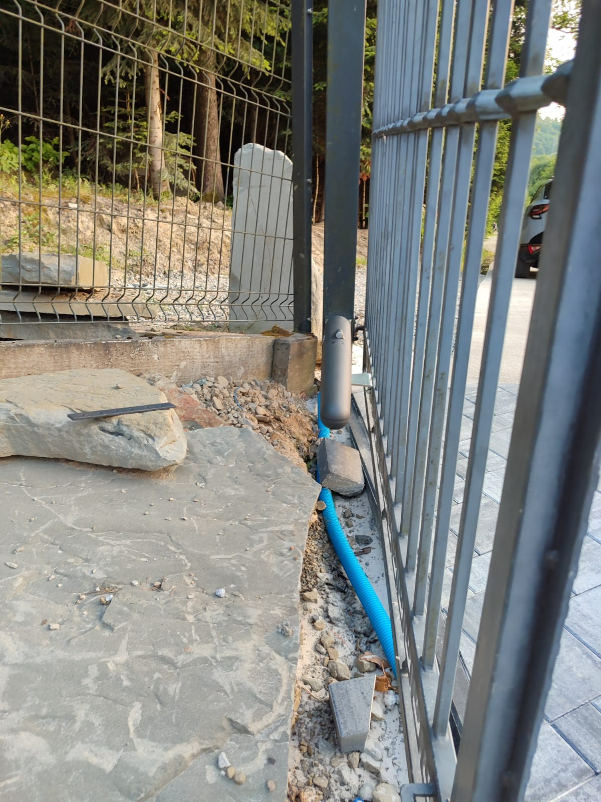 Montaż automatyki do bramy przesuwnej w Nowym Sączu. Widoczna szara brama, niebieski peszel z okablowaniem i elementy montażowe w surowym stanie.