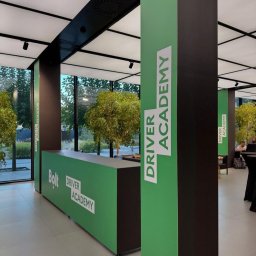 OKLEJWSZYSTKO.PL - Wnętrze biura Bolt Driver Academy z zielonymi elementami identyfikacji wizualnej, widoczne logo i nazwa akademii na ladzie recepcyjnej i filarach.