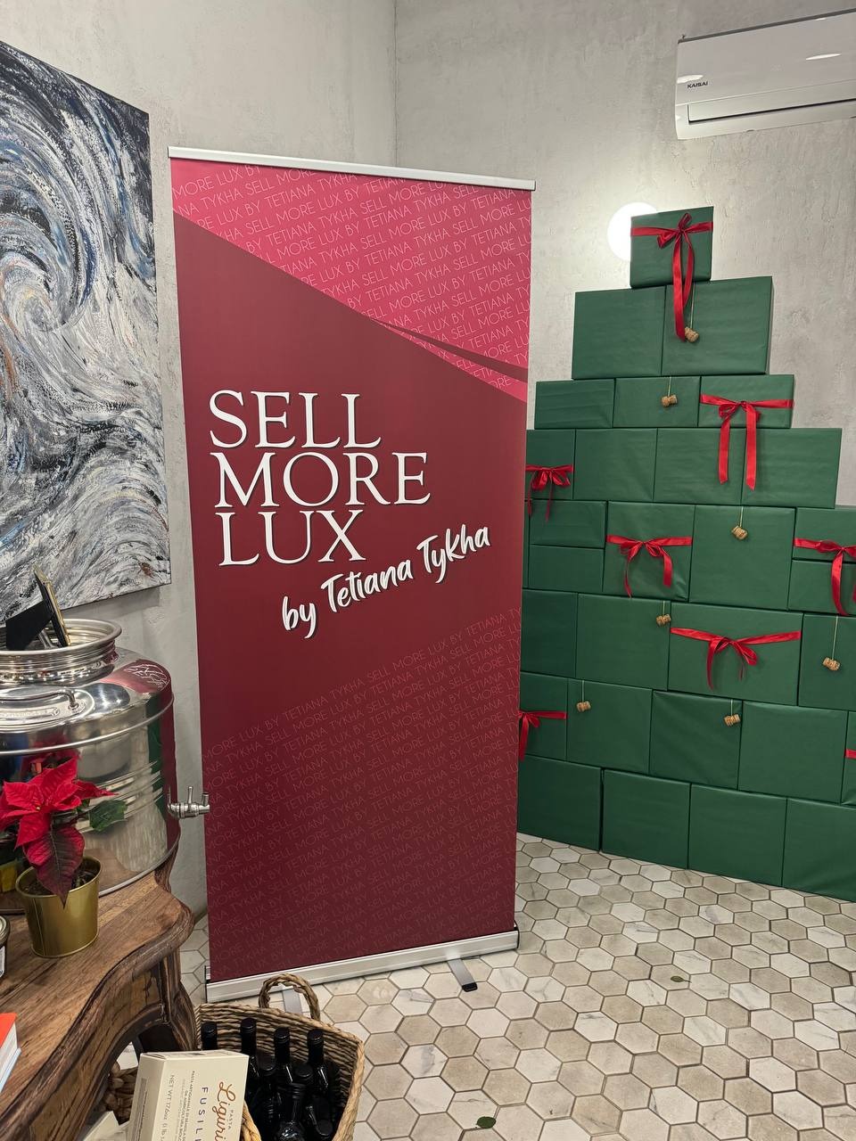 Roll-up z logo 'Sell More Lux by Tetiana Tykha' w biurze w Krakowie. Obok dekoracja z prezentów ułożonych w kształt choinki, tworząca świąteczny klimat.
