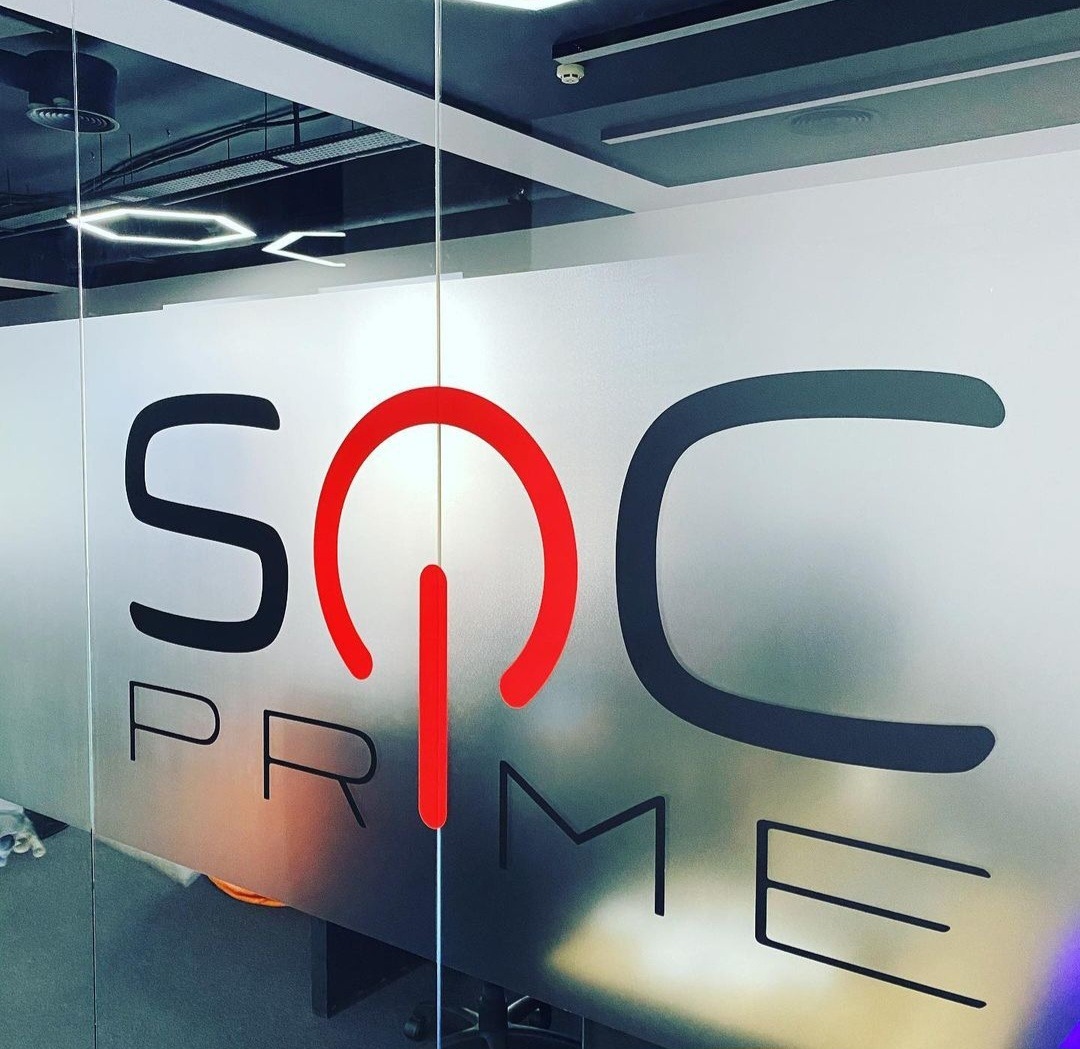 Oklejona szyba w biurze z logo 'SOC PRIME' w kolorach czarnym i czerwonym. Matowa folia tworzy efekt prywatności. Widoczne elementy sufitu.