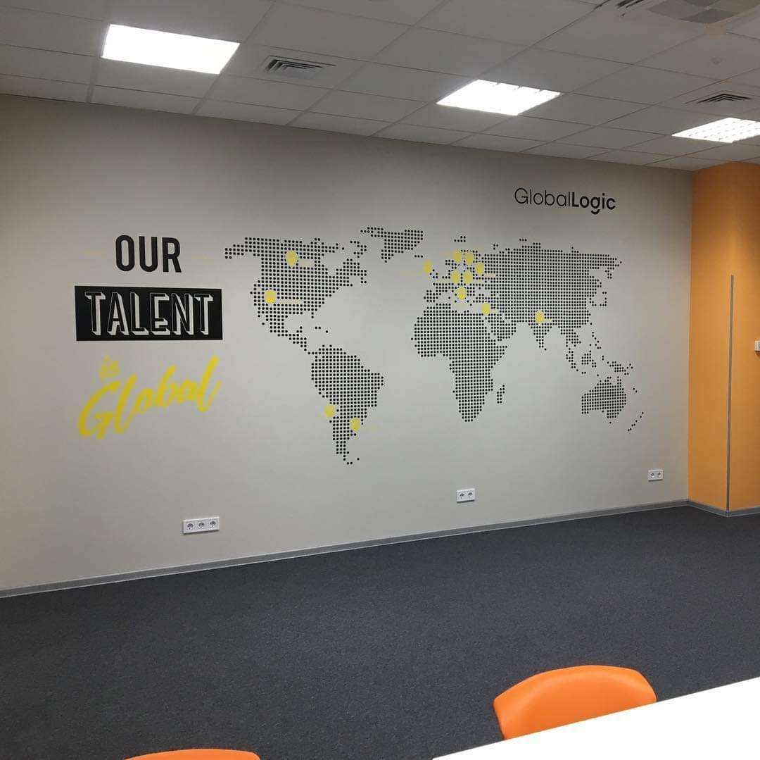 Ściana biura z mapą świata z kropek, napisy 'OUR TALENT' i logo firmy GlobalLogic. Żółte akcenty na mapie i w napisie.