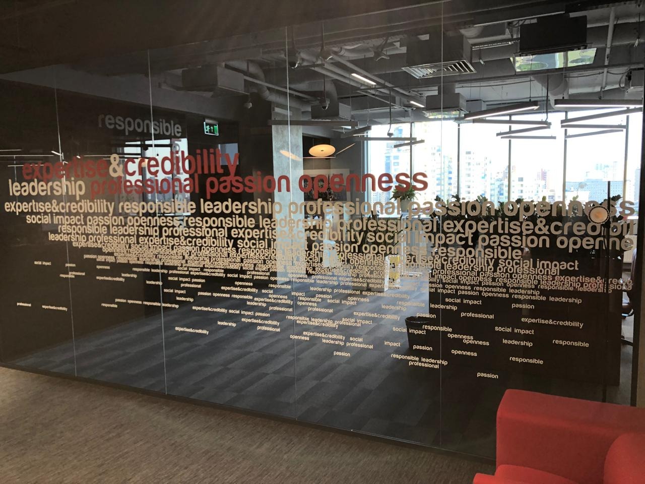 Szklana ściana biura z napisem 'expertise&credibility', 'leadership', 'passion', 'openness' w różnych rozmiarach i kolorach, widok na miasto w tle.