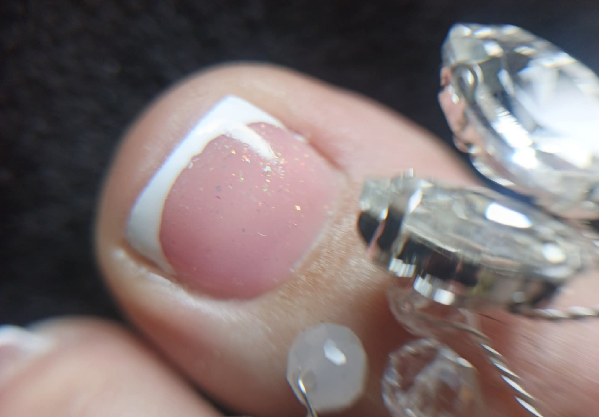 Powiększenie paznokcia u stopy z french manicure i delikatnymi drobinkami brokatu, ozdobionego biżuterią z kryształkami, prezentacja detalu pedicure.