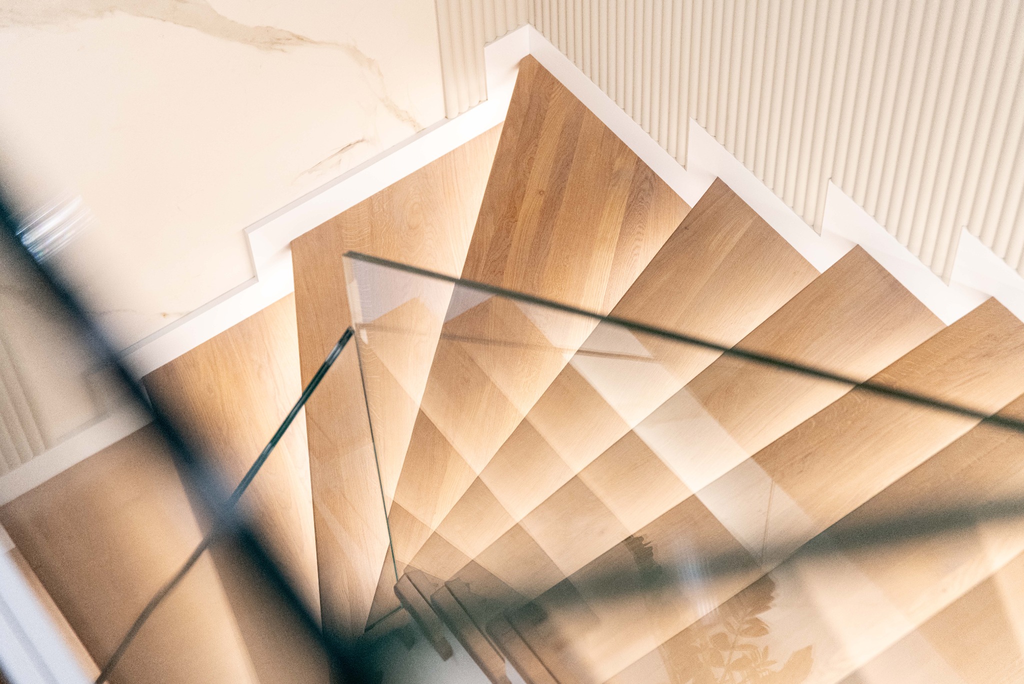 Nowoczesne schody drewniane z przeszkloną balustradą, widok z góry, ukazujący geometryczny układ stopni i minimalistyczne wykończenie.