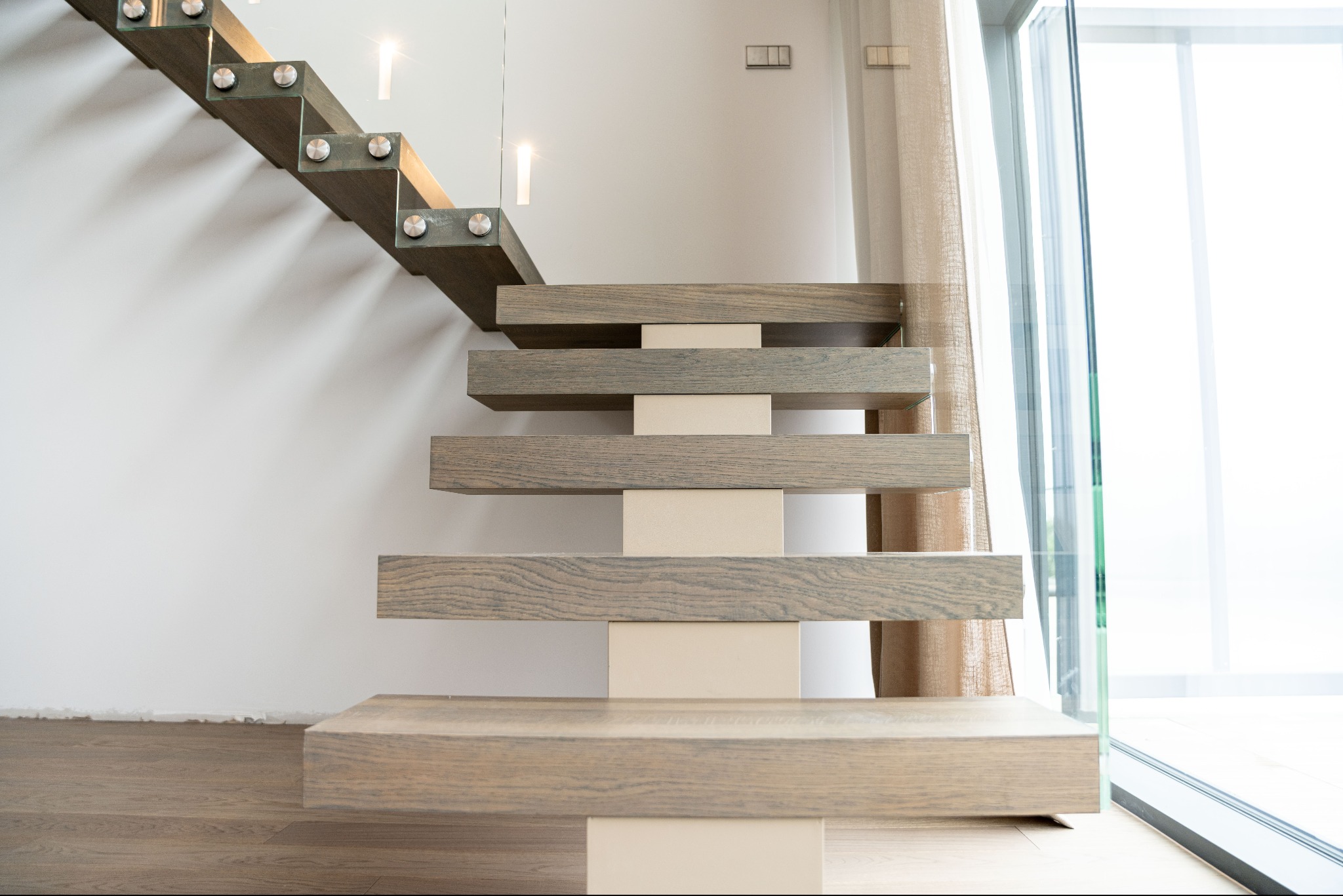 Nowoczesne schody wspornikowe z drewna z oświetleniem punktowym, minimalistyczny design, neutralna kolorystyka, widok od dołu na jasne wnętrze.