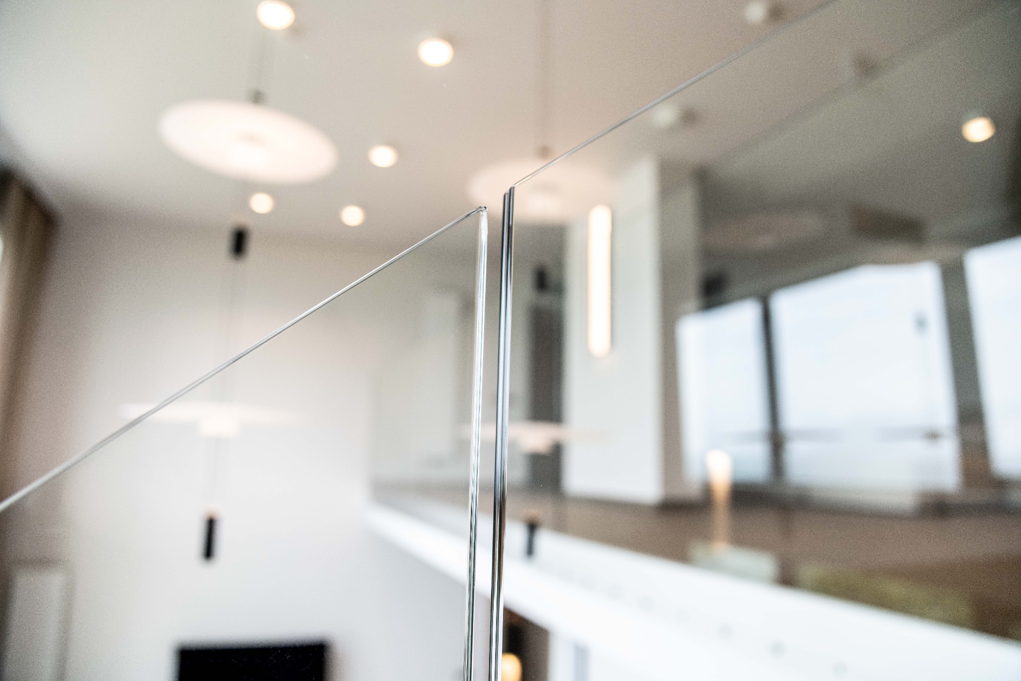 Szklana balustrada schodowa z metalowymi mocowaniami, widok z bliska na łączenie tafli szkła, nowoczesne oświetlenie w tle.