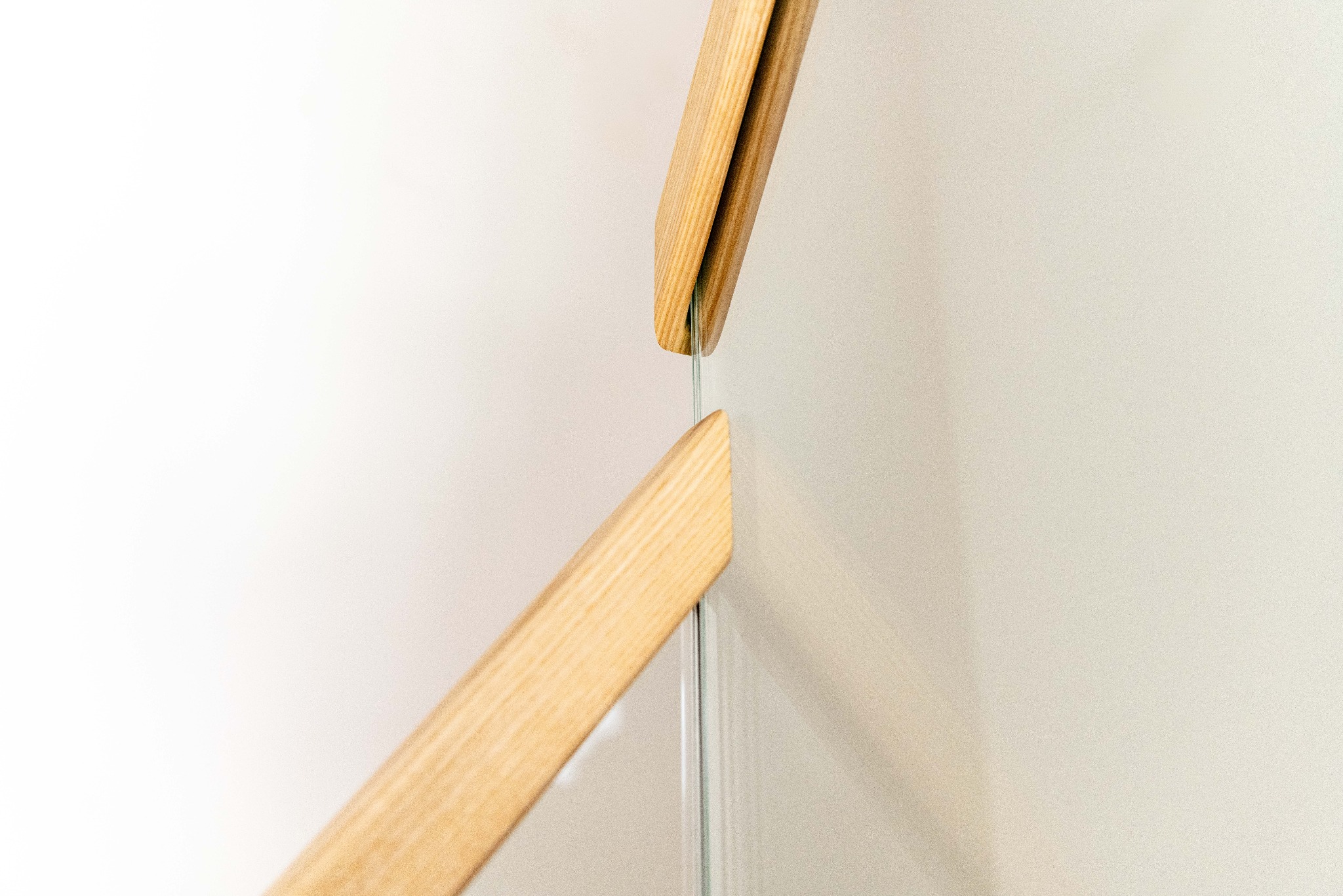 Fragment nowoczesnych schodów z drewnianą poręczą i szklaną balustradą, minimalistyczny design, jasne tło, detal poręczy.