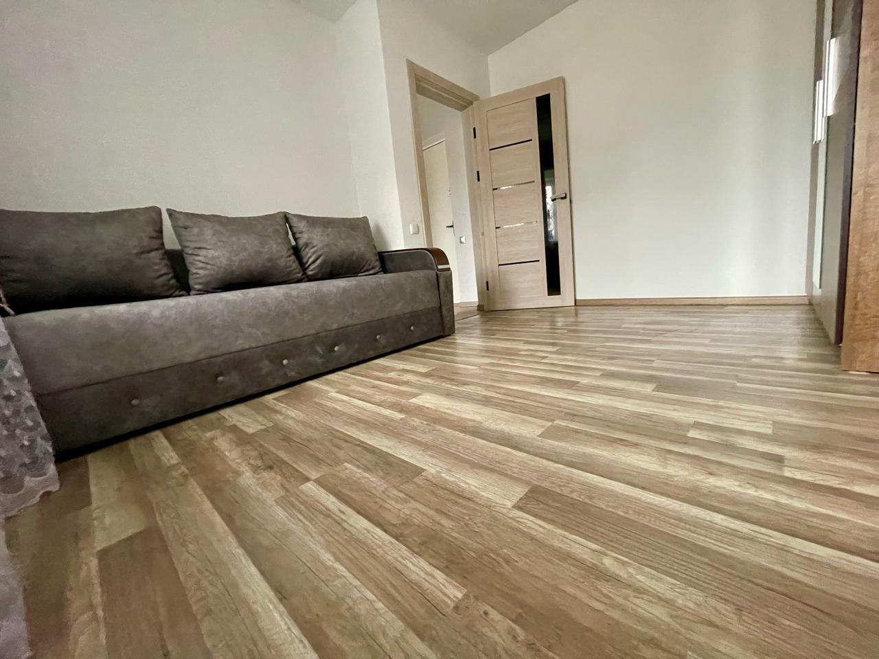 Jasne panele podłogowe w pokoju z szarą kanapą i dwiema parami drzwi. Widok na wykończone wnętrze z niskiego kąta.