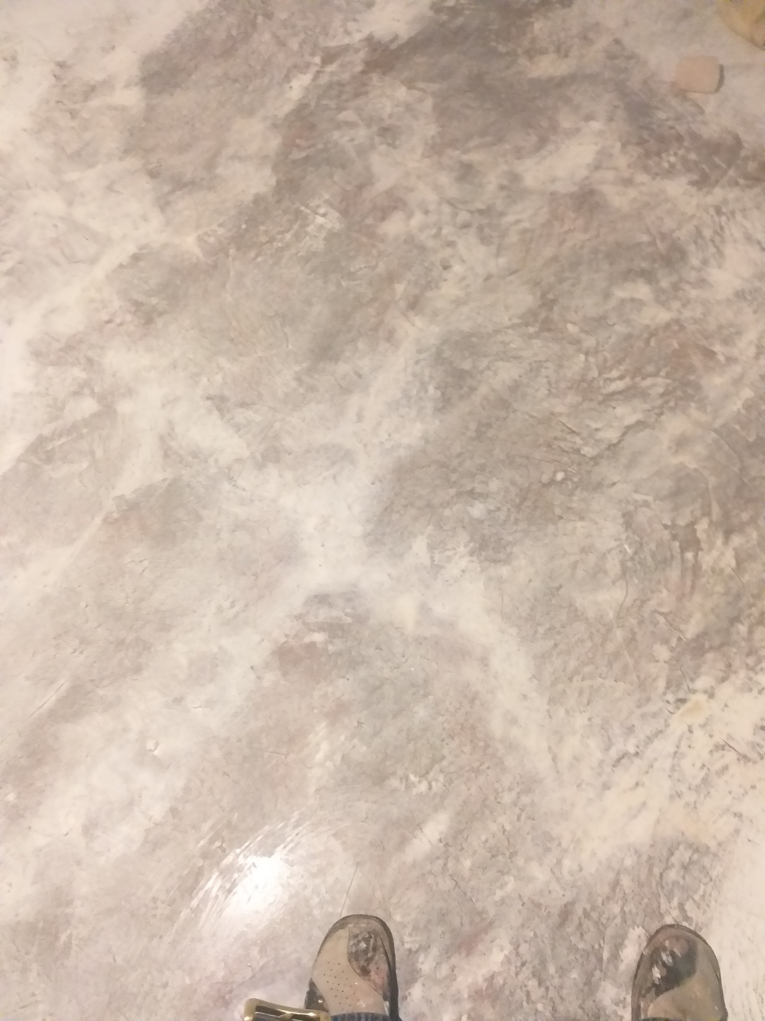 Jasnoszara, wzorzysta posadzka z mikrocementu w stylu industrialnym, widoczne fragmenty butów osoby stojącej na powierzchni. Efekt końcowy po wykończeniu.