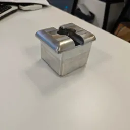 Metalowy prototyp z wyraźnymi śladami obróbki skrawaniem, na białym biurku w Warszawie. Widoczne warstwy materiału i charakterystyczny kształt otworu.