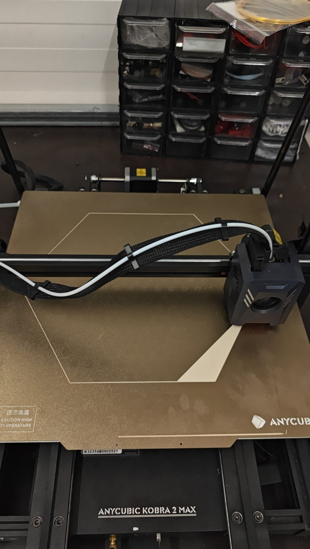Drukarka 3D Anycubic Kobra 2 Max w trakcie pracy, widoczna głowica drukująca i powstający model na platformie roboczej. W tle organizer z akcesoriami.
