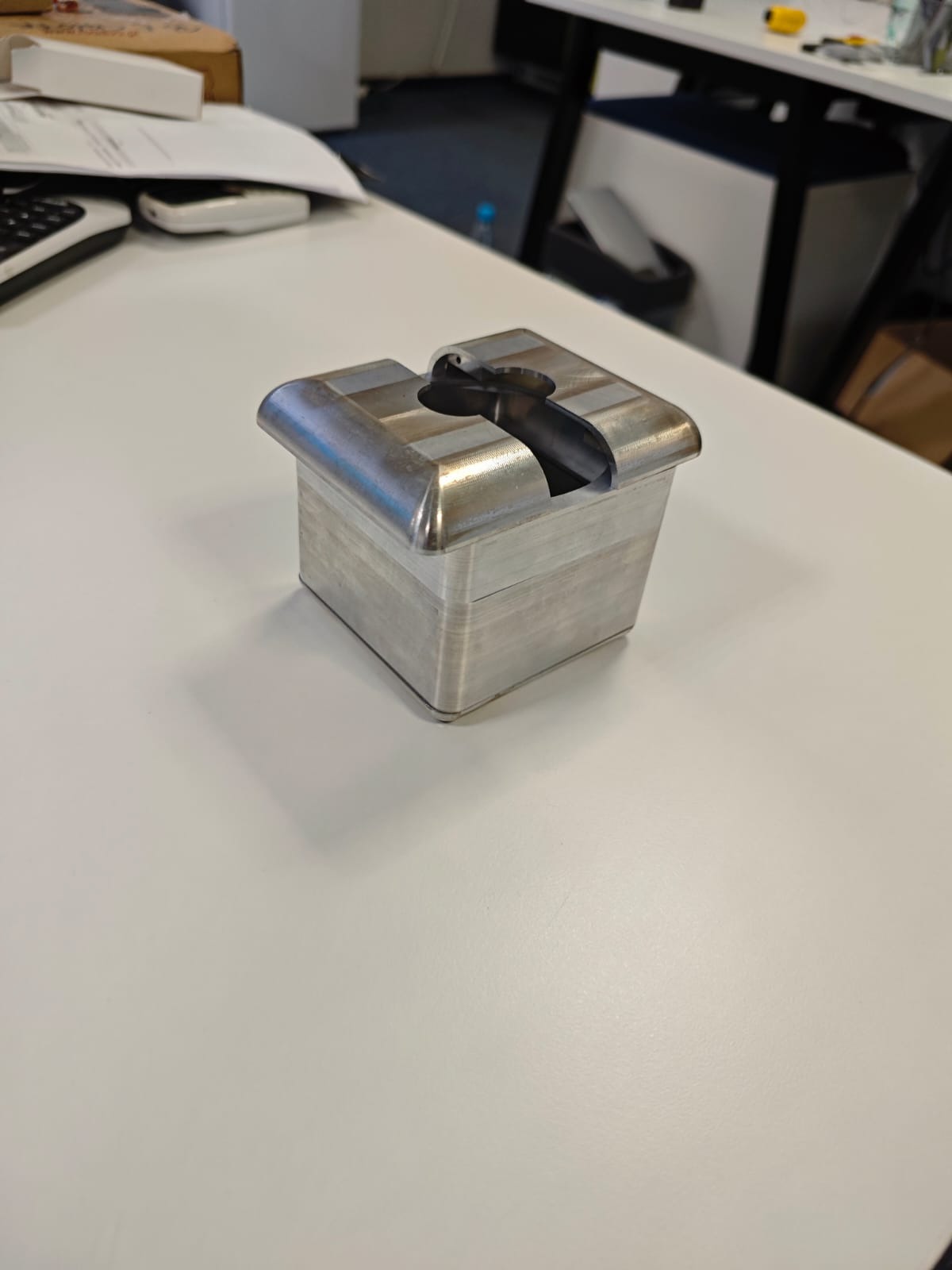 Metalowy prototyp z wyraźnymi śladami obróbki skrawaniem, na białym biurku w Warszawie. Widoczne warstwy materiału i charakterystyczny kształt otworu.