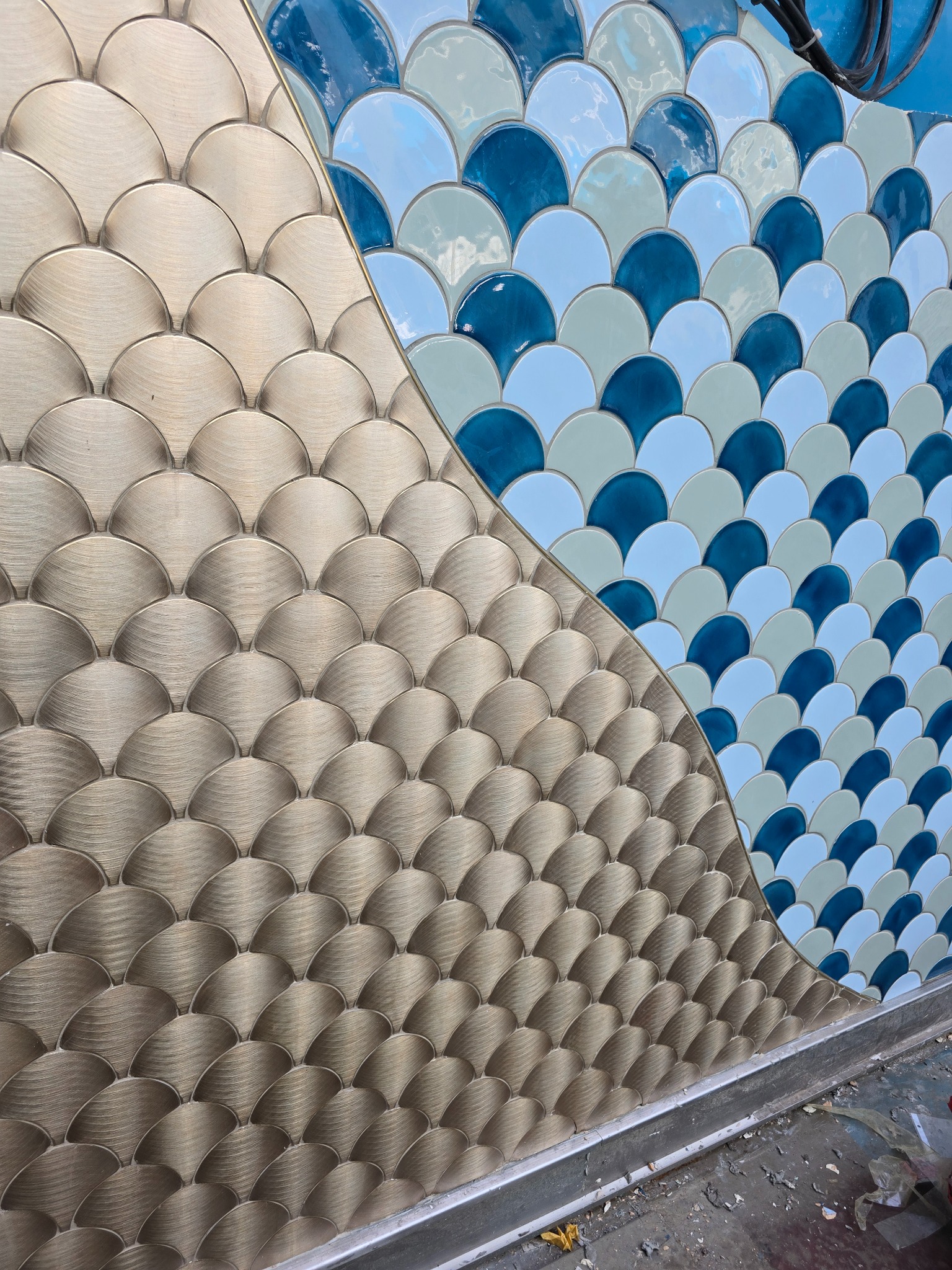 Mozaika w kształcie rybiej łuski, łącząca złote i niebieskie odcienie, ułożona na ścianie w Żarki-Letnisko. Dekoracyjne wykończenie wnętrz.