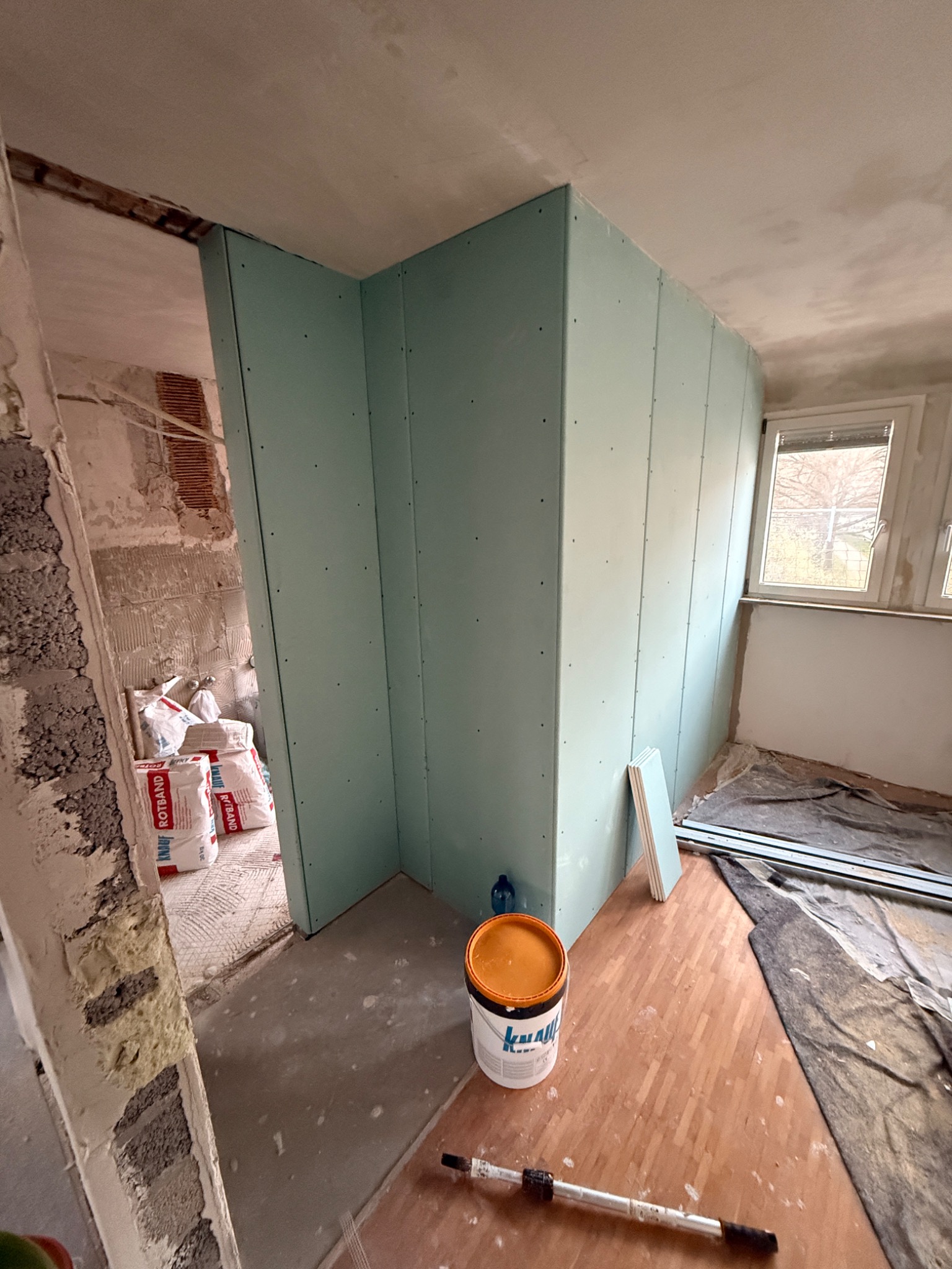 Montaż ścianki działowej z płyty karton gips w trakcie remontu mieszkania. Widoczne płyty GK, worki z zaprawą, wiadro z klejem i narzędzia.