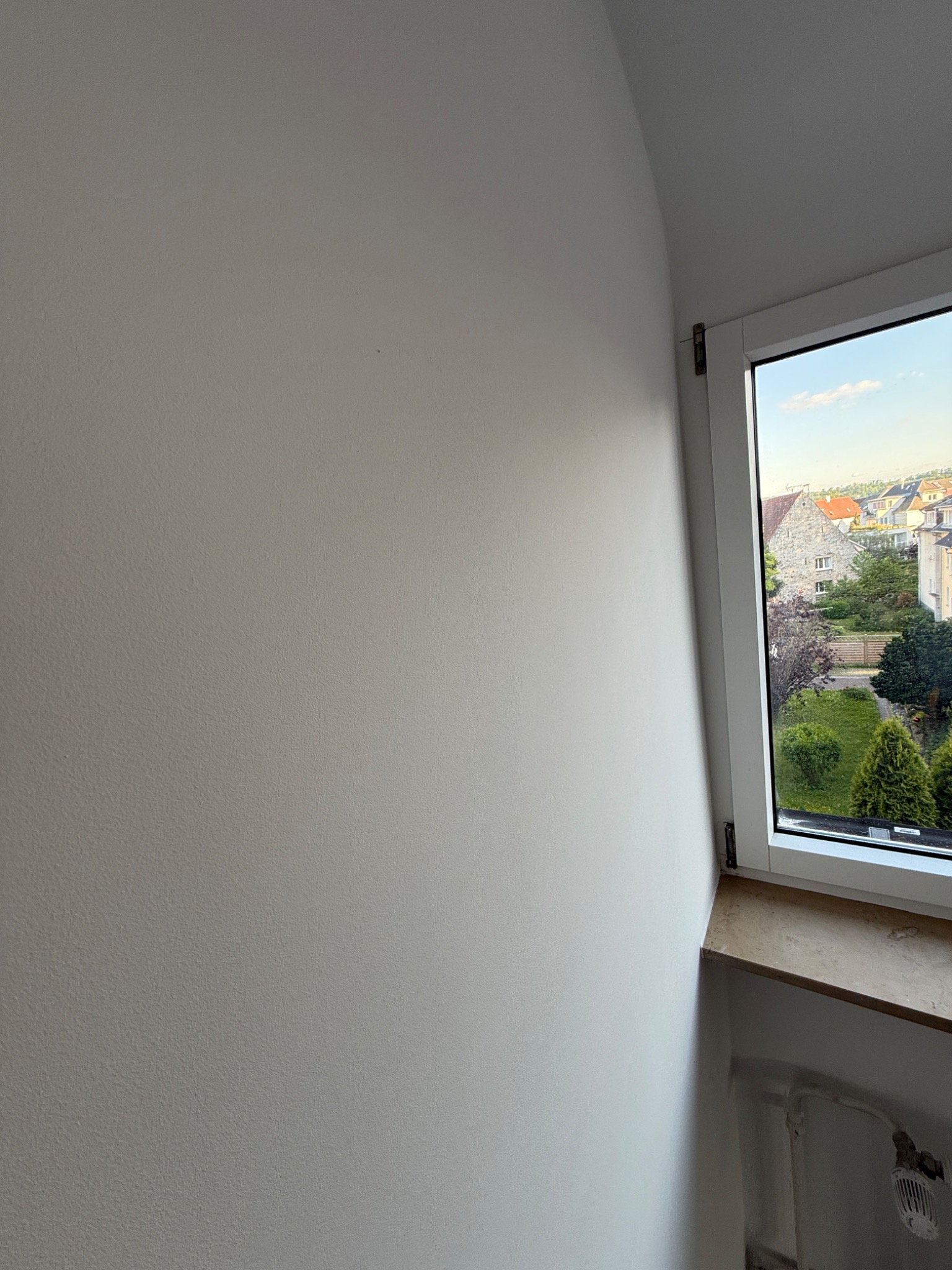 Ściana po szpachlowaniu i malowaniu na biało, widok na zielony ogród przez okno. Świeżo wykończone wnętrze.