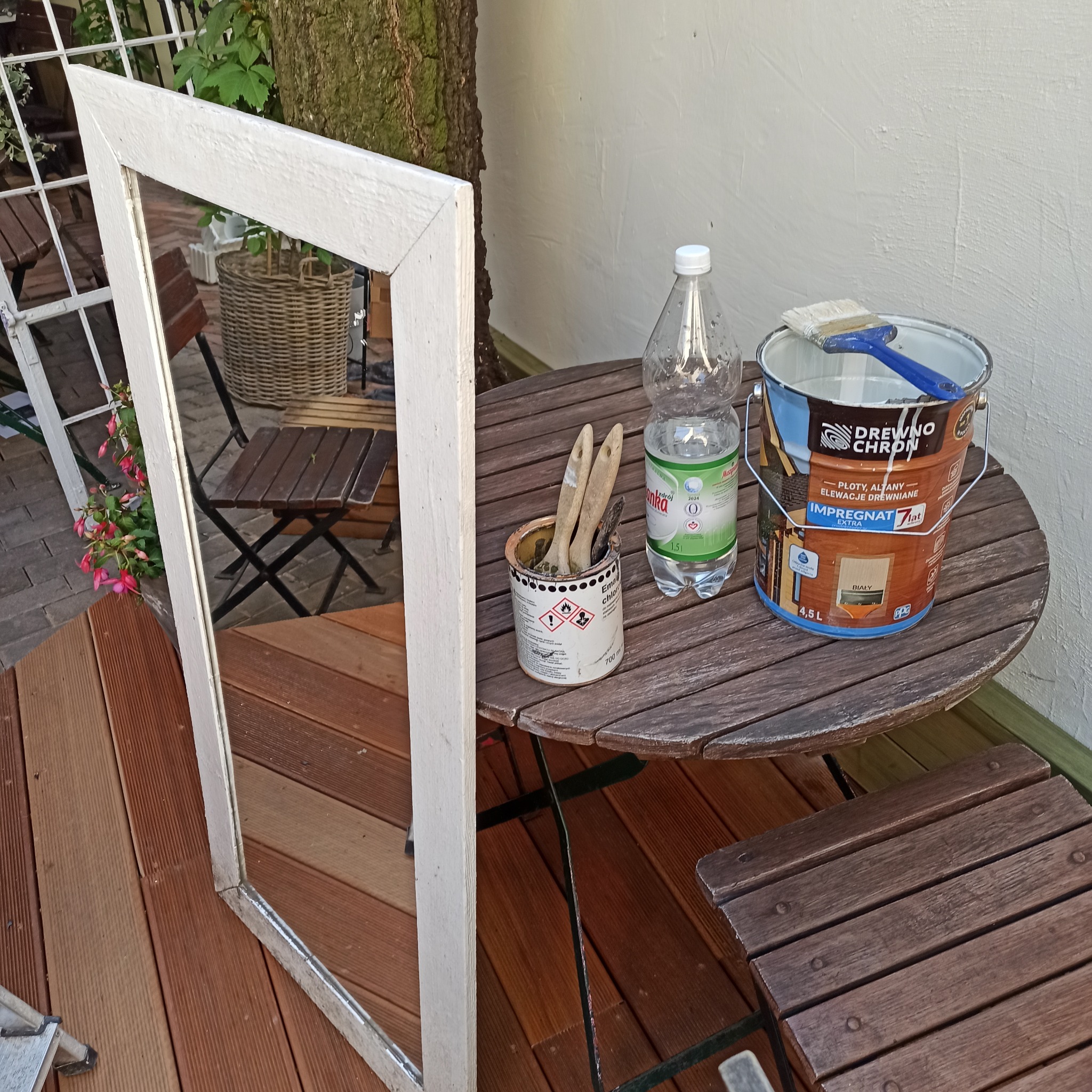 Impregnat do drewna, pędzle i rama okienna na drewnianym stoliku w ogrodzie, gotowe do malowania. Prace przygotowawcze przed malowaniem elementów drewnianych.