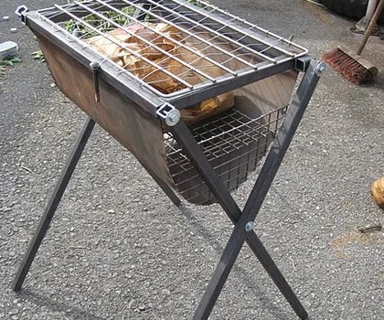 Metalowy grill z rusztem i koszem na węgiel, spawany z profili, na zewnątrz, widoczne ślady użytkowania i niedoskonałości spoin.