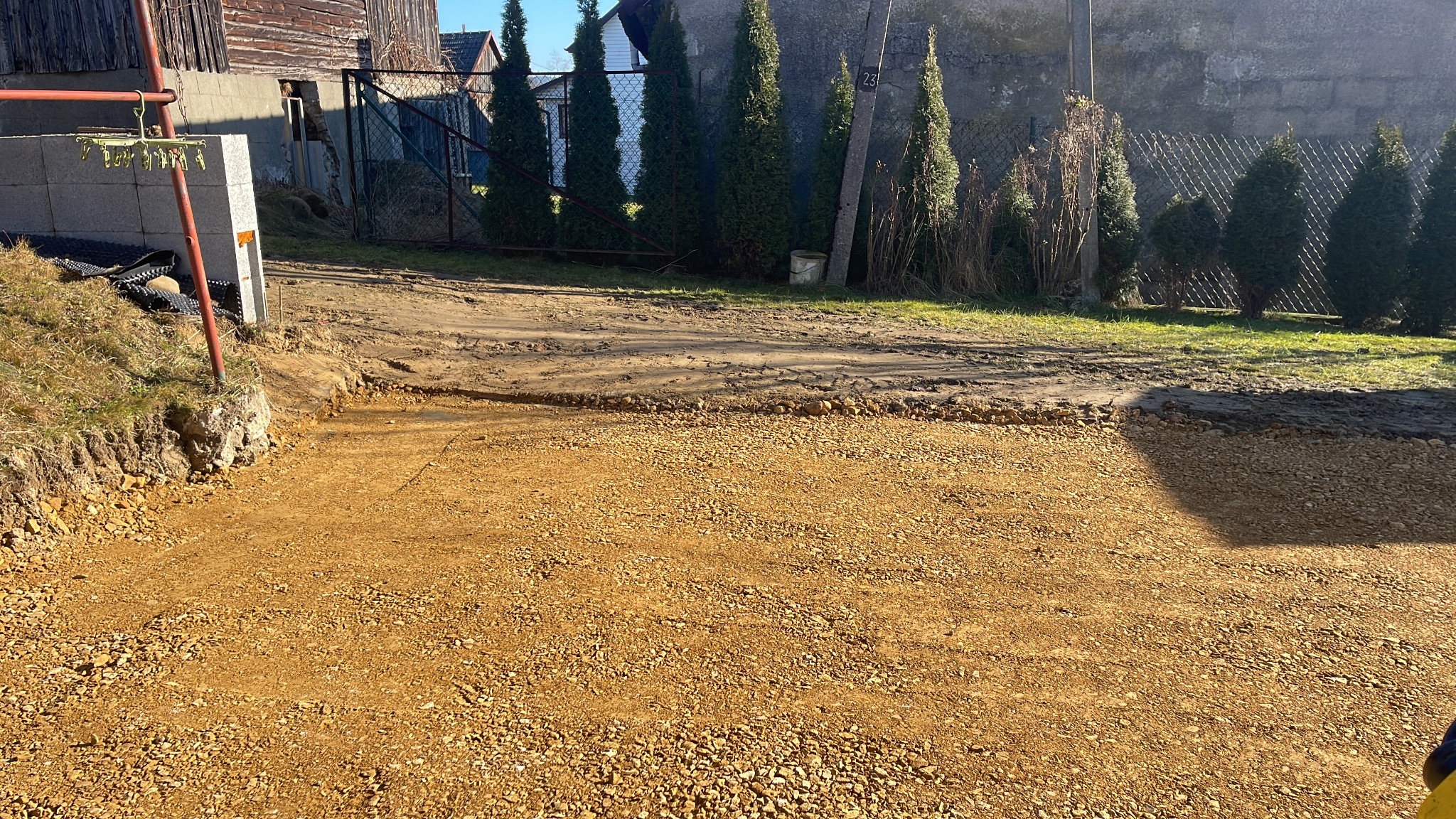 Przygotowany teren pod kostkę brukową z podsypką, widoczne obrzeża i częściowo ułożona kostka. W tle tuje i ogrodzenie posesji.