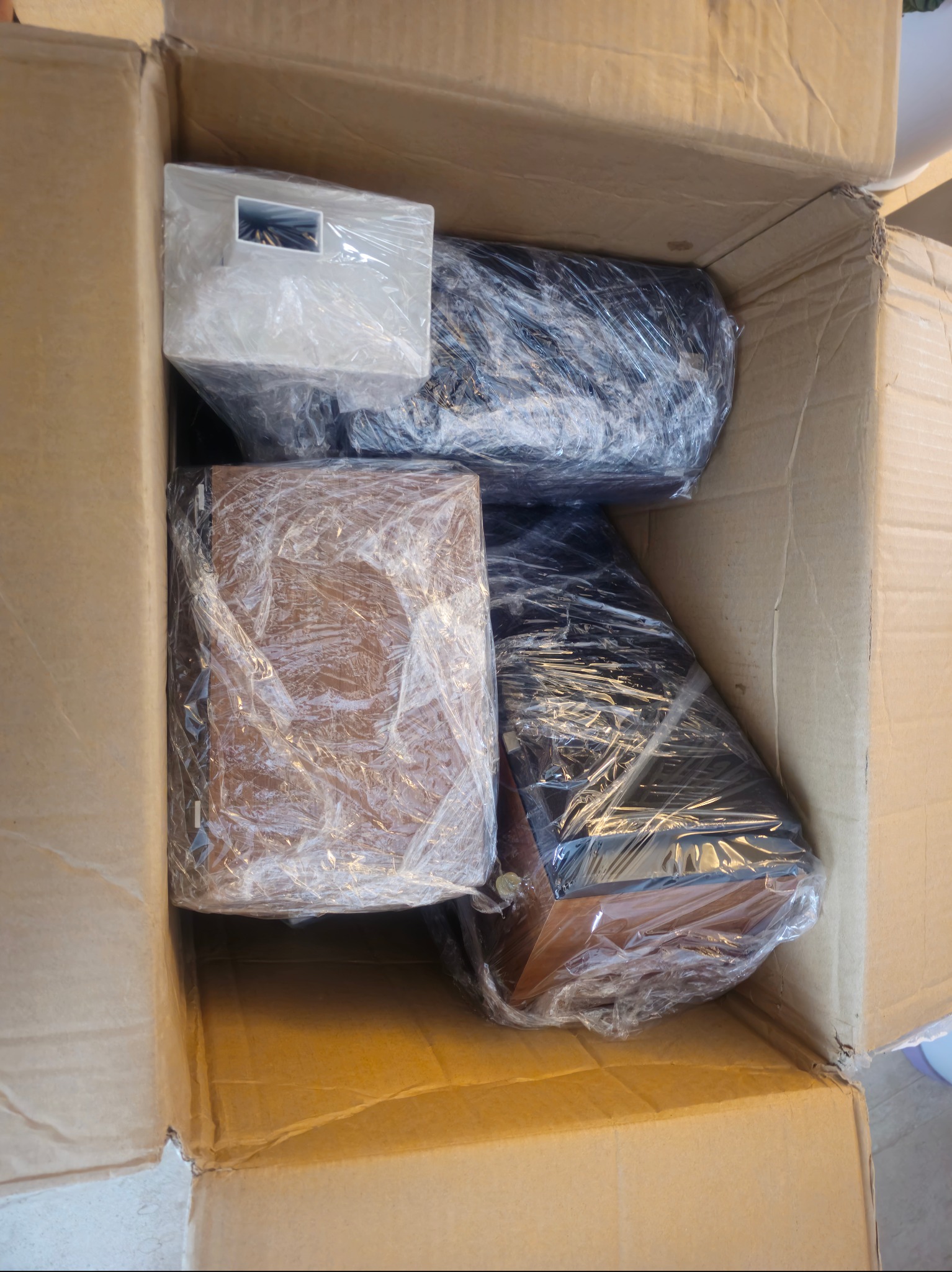 Kartonowe pudło wypełnione różnymi zapakowanymi przedmiotami, zabezpieczonymi folią stretch przed transportem. Widok z góry.