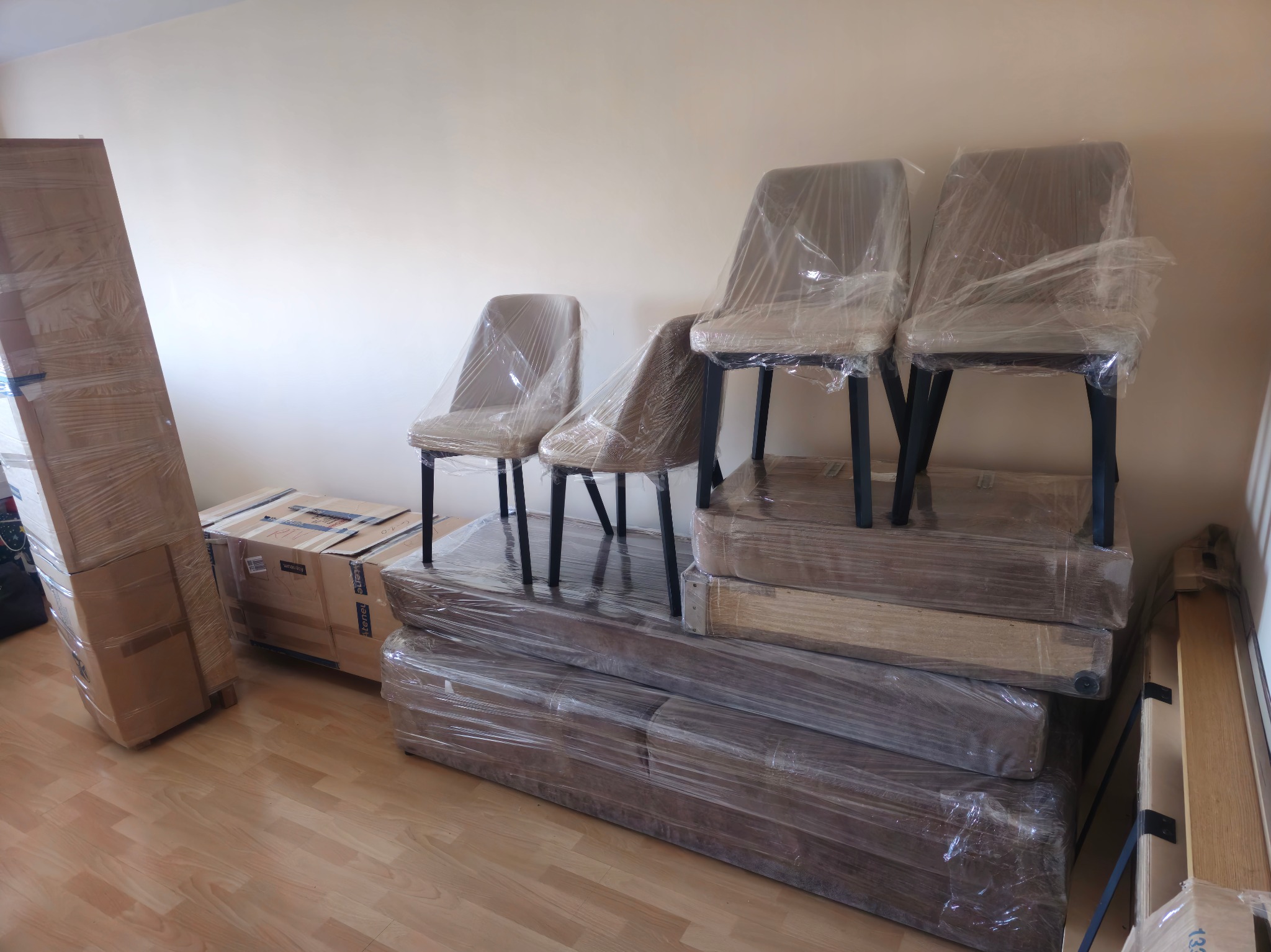 Spakowane meble (krzesła, kartony) owinięte folią ochronną, przygotowane do transportu podczas przeprowadzki. Ułożone w stos na podłodze.