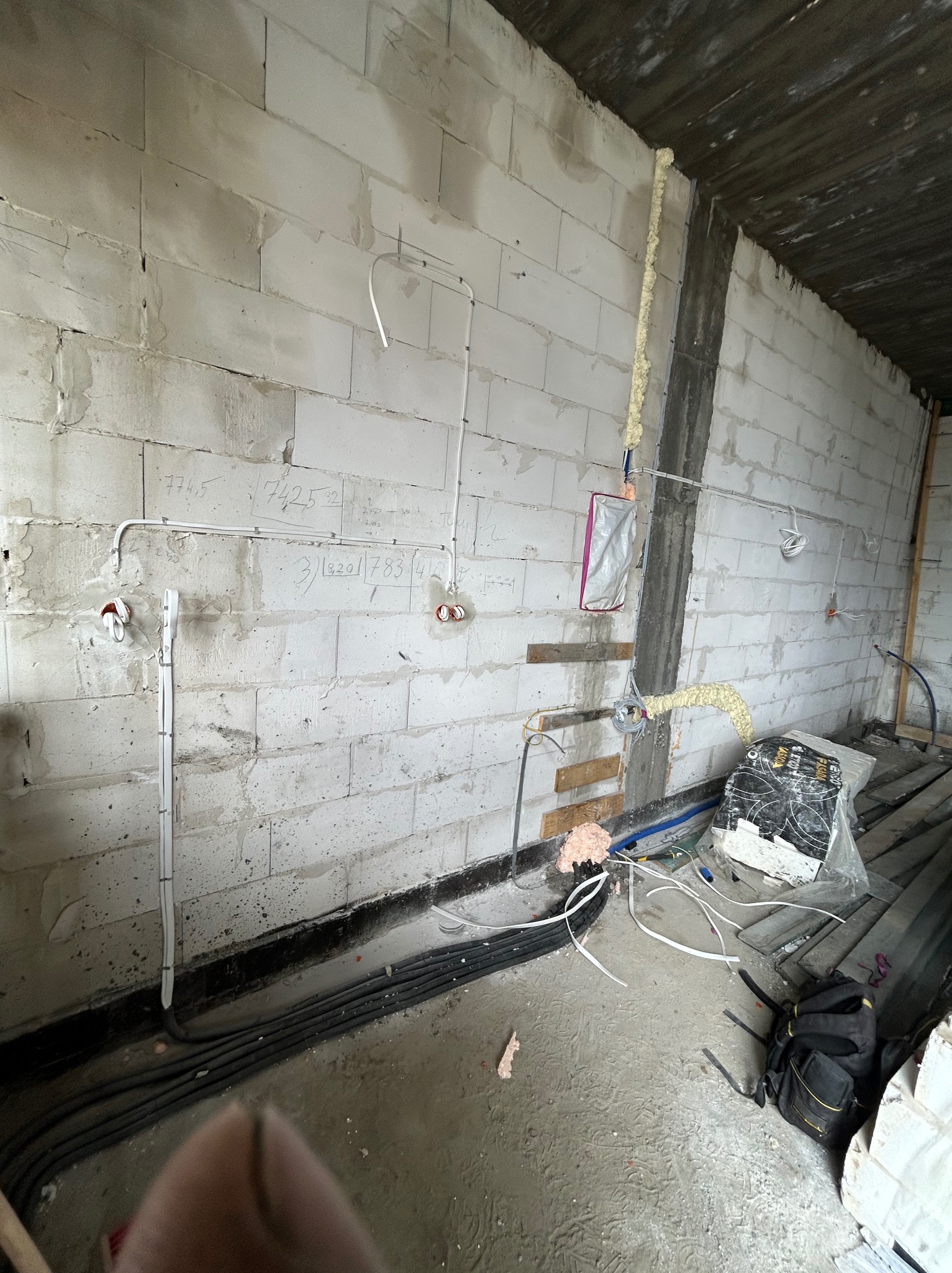 Surowe wnętrze w trakcie prac elektrycznych: kable, puszki instalacyjne, pianka montażowa przy ścianie z betonu komórkowego, instalacja elektryczna w trakcie montażu.