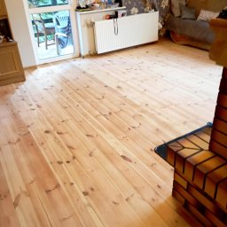 Pokój po cyklinowaniu deski sosnowej pokrytej wpierw starym brązowym lakierem z licznymi plamami i rysami 