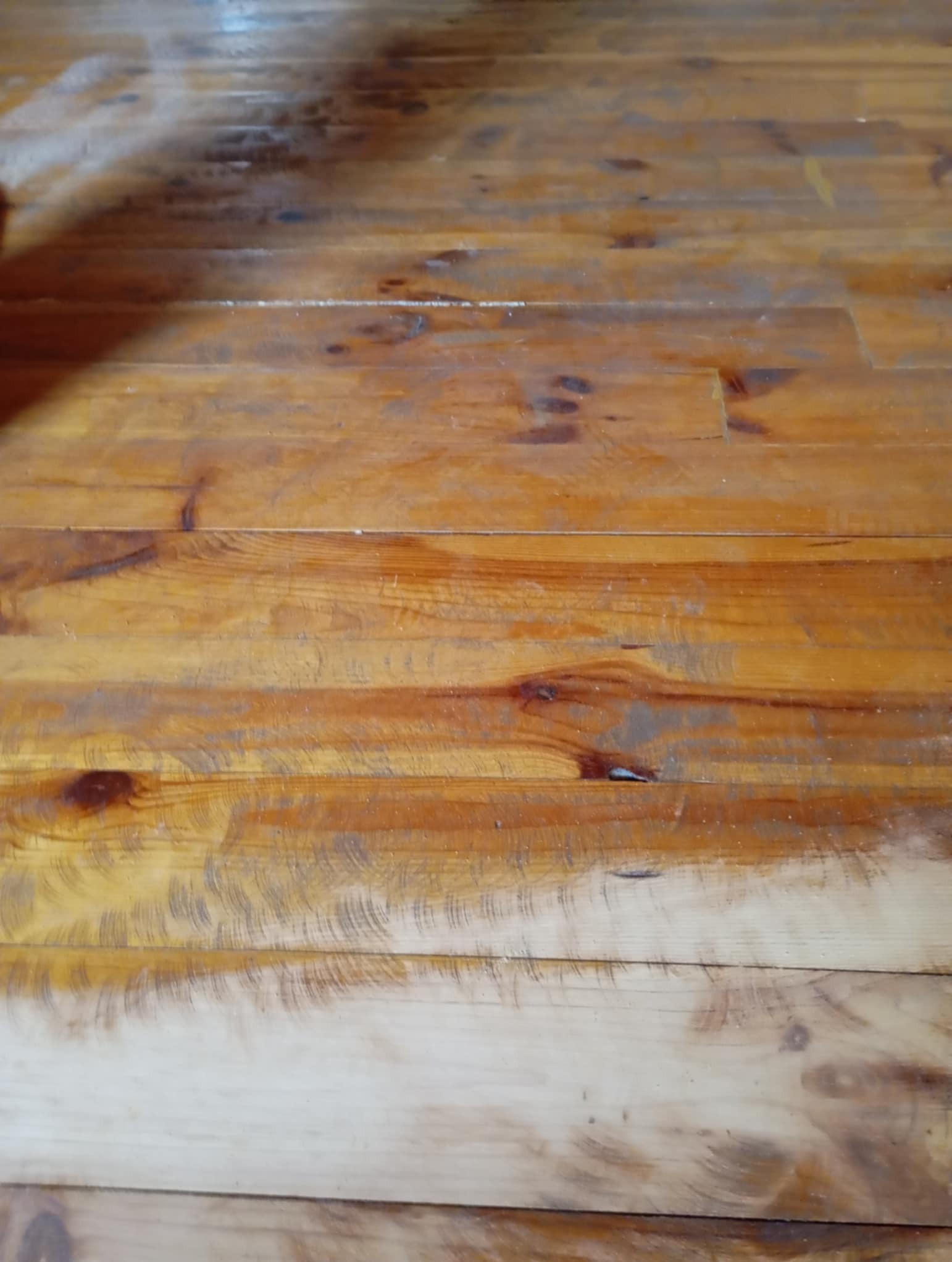 Uszkodzona, sosnowa podłoga na poddaszu z widocznymi rysami, ciemnym lakierem i śladami po nieudanym czyszczeniu, ukazująca wyzwanie przed renowacją.