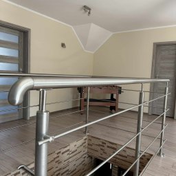 Dominika Zborowska - Nowoczesna balustrada nierdzewna na antresoli z widokiem na dół, z dekoracyjną okładziną ścienną. W tle widoczny stół do piłkarzyków.