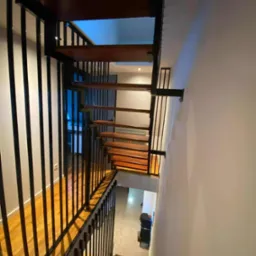 Nowoczesne schody z drewnianymi stopniami i czarną metalową balustradą, widok z góry, podkreślający minimalistyczny design i solidne wykonanie.