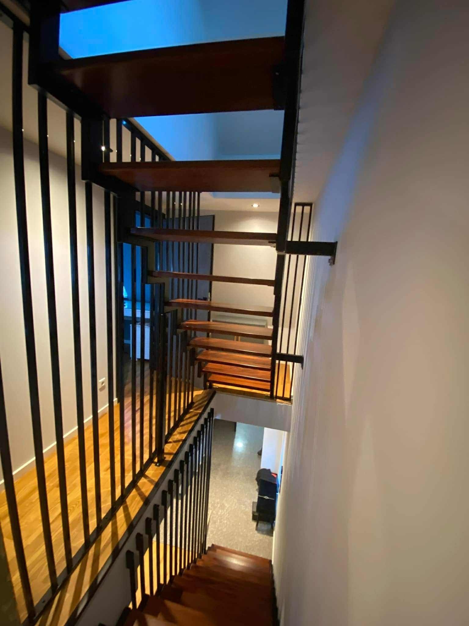 Nowoczesne schody z drewnianymi stopniami i czarną metalową balustradą, widok z góry, podkreślający minimalistyczny design i solidne wykonanie.