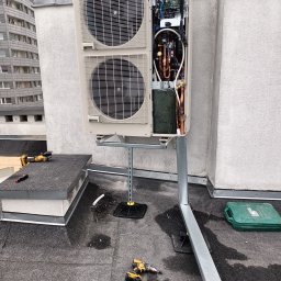 SG INSTALACJE SEBASTIAN GOSEK - Klimatyzator na dachu budynku, zamontowany na metalowej konstrukcji. Widoczne narzędzia pracy, skrzynka narzędziowa. Otwarta obudowa klimatyzatora eksponuje elementy wewnętrzne.