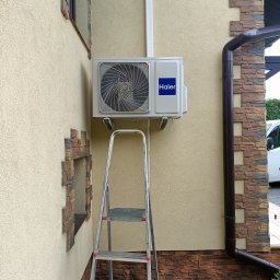 SG INSTALACJE SEBASTIAN GOSEK - Zamontowana klimatyzacja Haier na elewacji budynku w Bielanach Dużych, widoczna drabina. Instalacja z rurami prowadzonymi po ścianie.