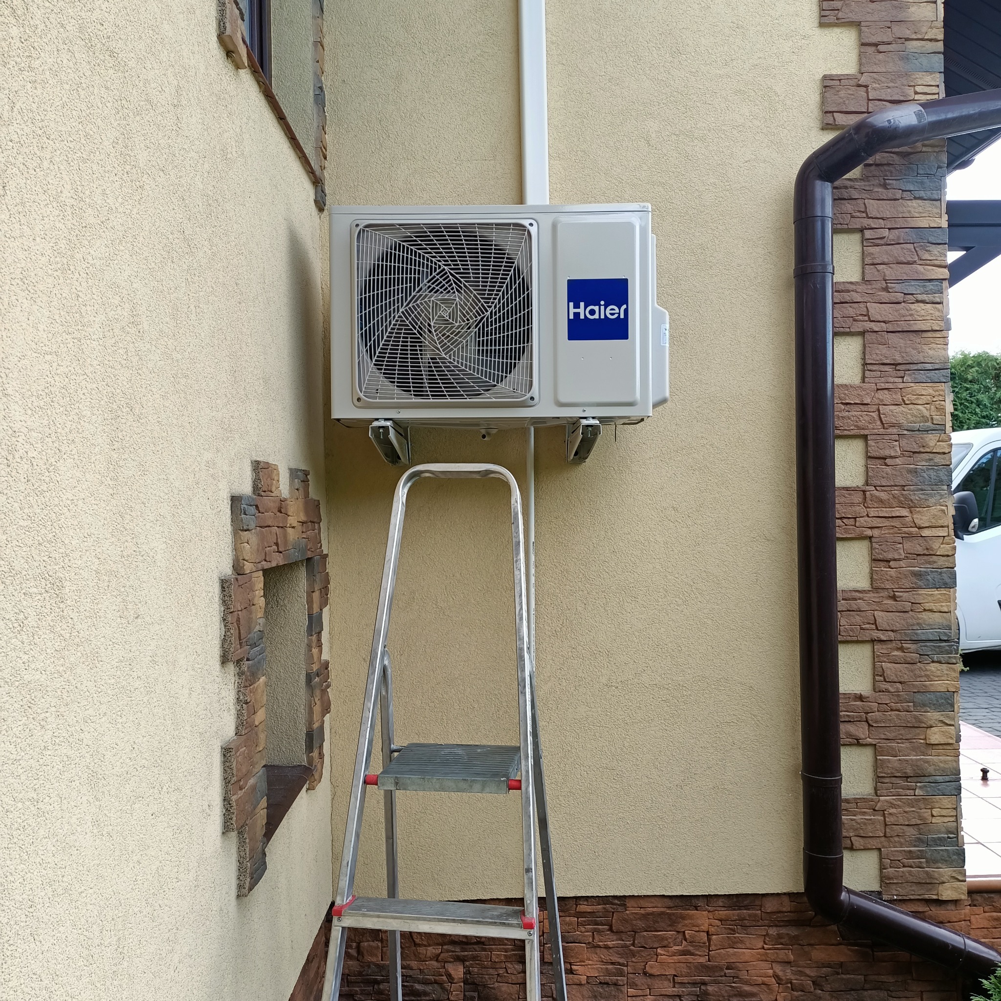 Zamontowana klimatyzacja Haier na elewacji budynku w Bielanach Dużych, widoczna drabina. Instalacja z rurami prowadzonymi po ścianie.