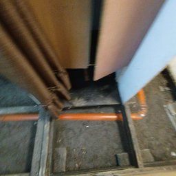 Fuszkin - Fragment podłogi z widocznymi pomarańczowymi rurami instalacji wodnej. Ujęcie z góry, z perspektywy osoby stojącej na podłodze.