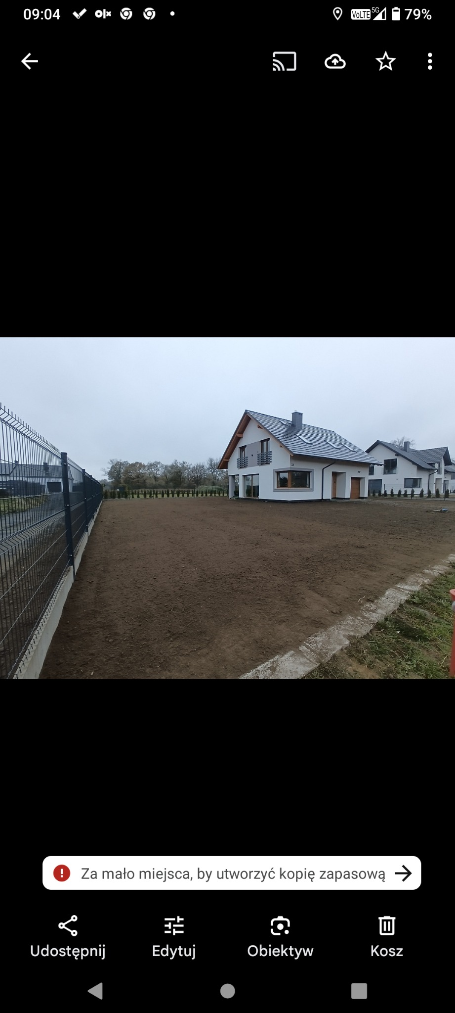 Wyrównany teren pod budowę z ogrodzeniem panelowym i widokiem na nowoczesne domy jednorodzinne. Przygotowanie działki pod przyszły ogród. Pochmurny dzień.