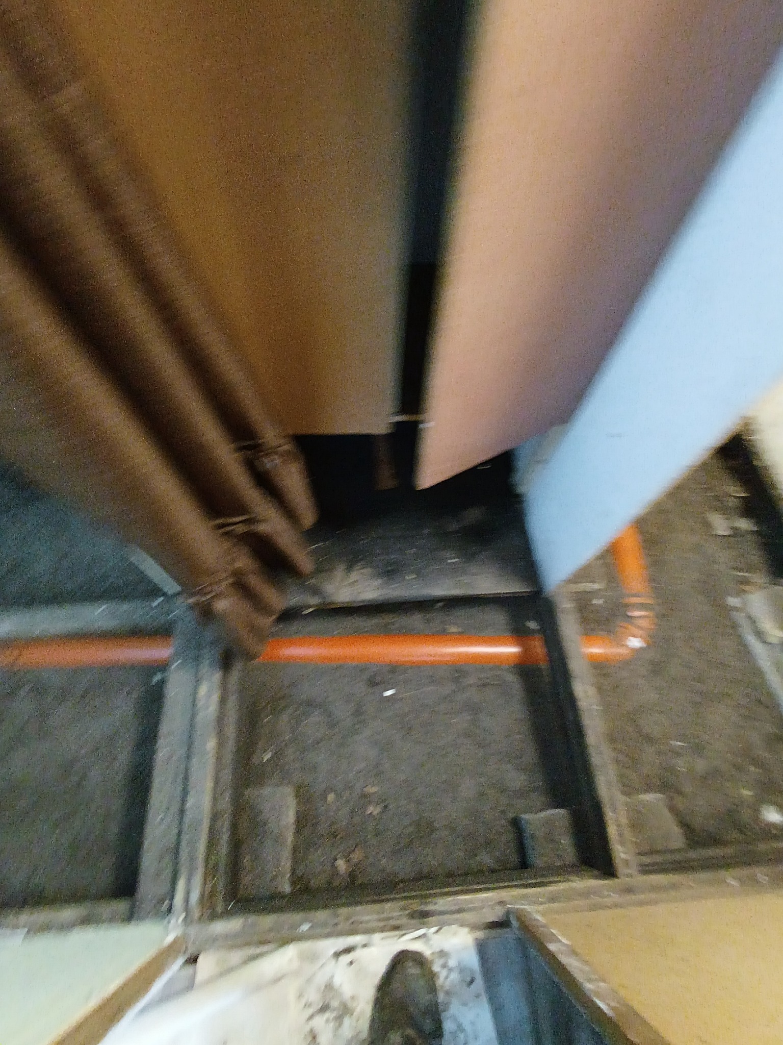 Fragment podłogi z widocznymi pomarańczowymi rurami instalacji wodnej. Ujęcie z góry, z perspektywy osoby stojącej na podłodze.