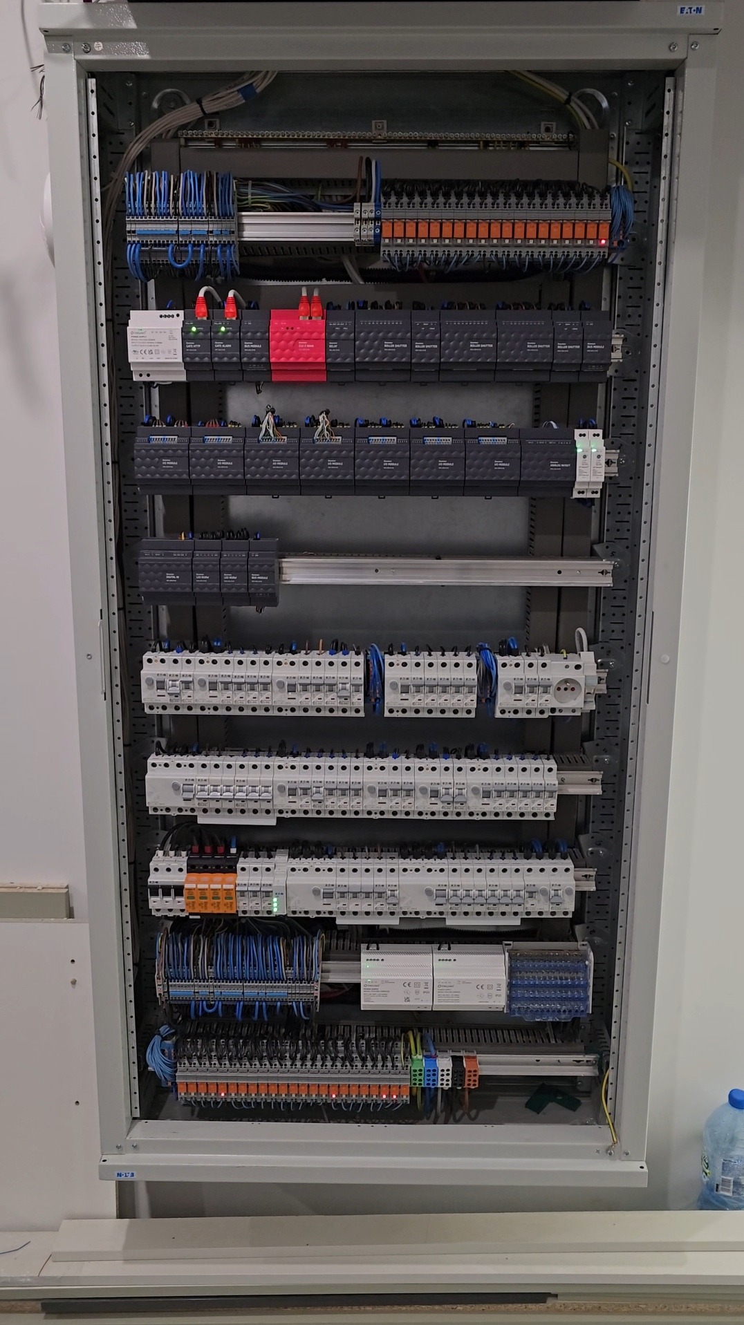 Rozdzielnica elektryczna w szafie, widoczne liczne moduły, kable i złącza. Elementy Eaton. Górna część szafy wypełniona przewodami i zabezpieczeniami. Dolna część zawiera listwy zaciskowe.