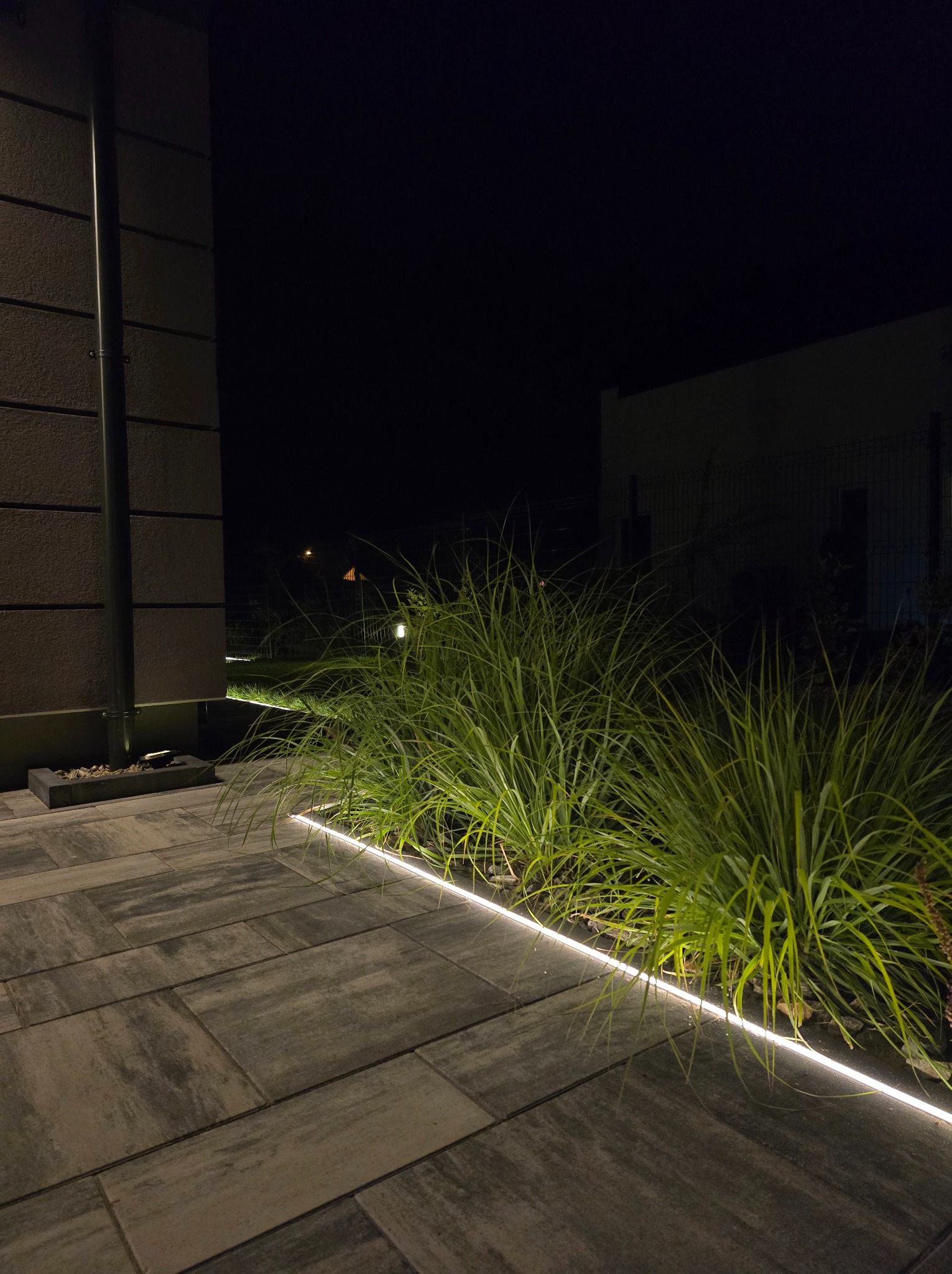 Oświetlenie LED wzdłuż ścieżki i rabaty w Wieńcu, tworzące nowoczesny akcent w ogrodzie nocą. Podświetlone trawy ozdobne i kostka brukowa.