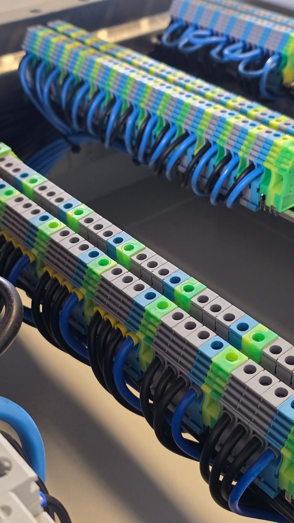 Szczegółowe ujęcie z góry: listwy zaciskowe z niebieskimi i czarnymi przewodami w rozdzielnicy, z akcentami zieleni i żółci. Element instalacji elektrycznej.